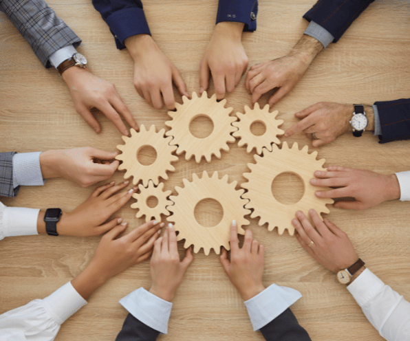 engineers hands reaching toward wooden gears on a work table; illustrating team work